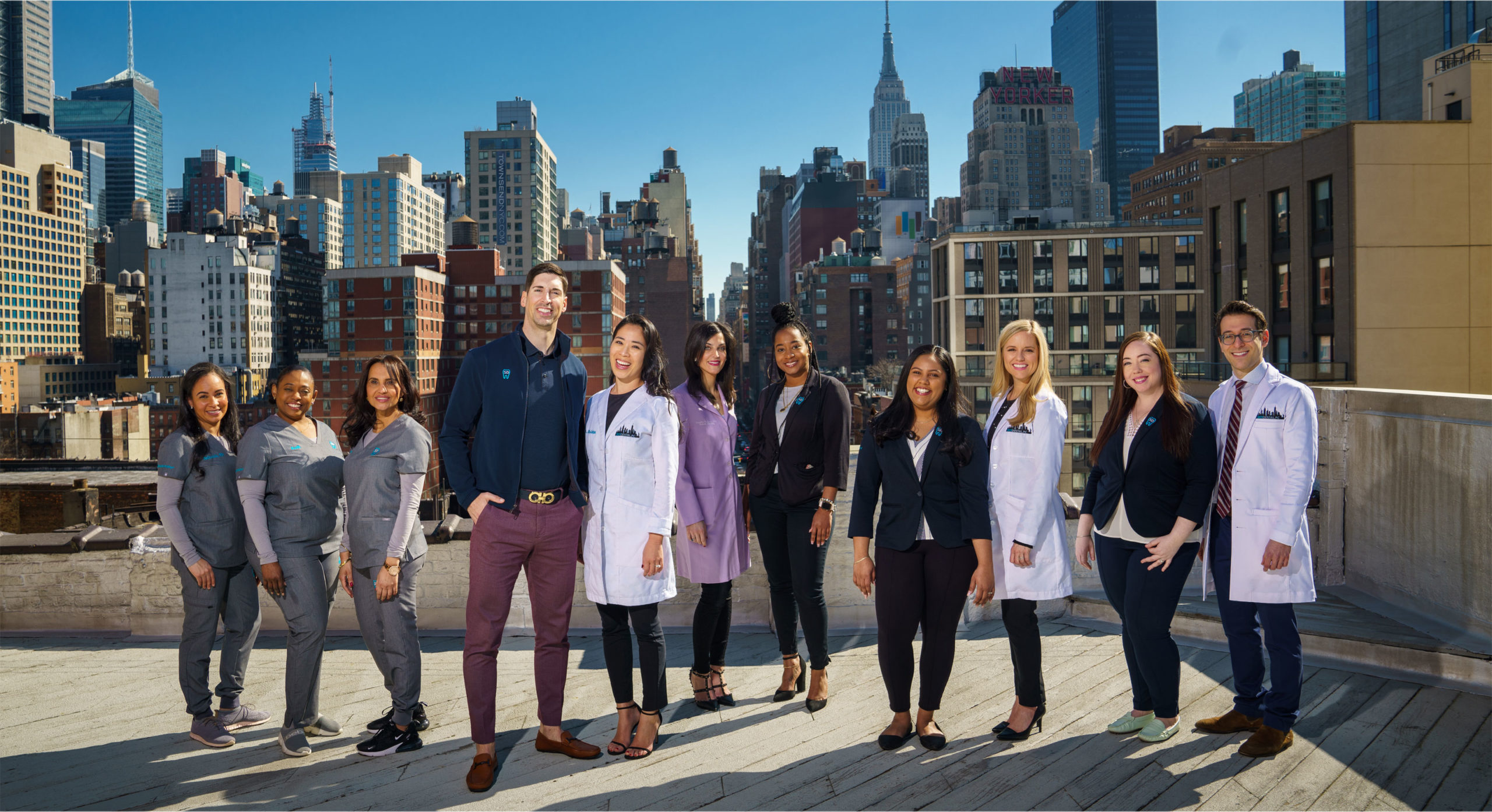 Team of SKY DENTAL NYC located in Fidi NYC posing for picture on the rooftop. Sunny day, blue sky, beautiful skyline in background.