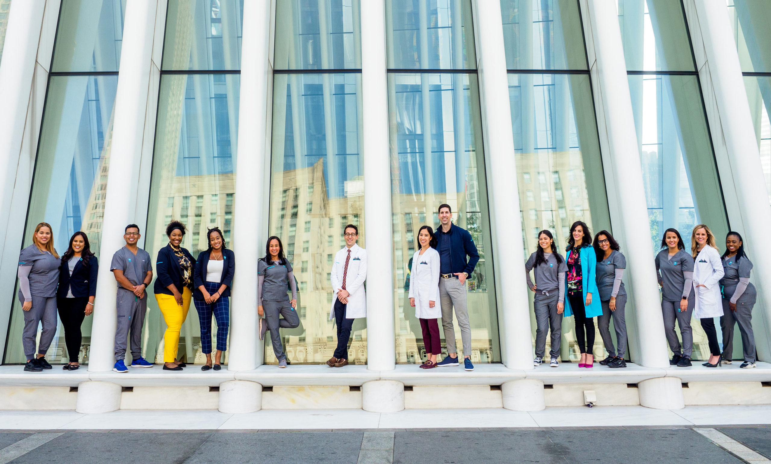 The Sky team poses outside the Oculus, framed by windows, in groups of two and three. Sky Dental, best dental practice in NYC.