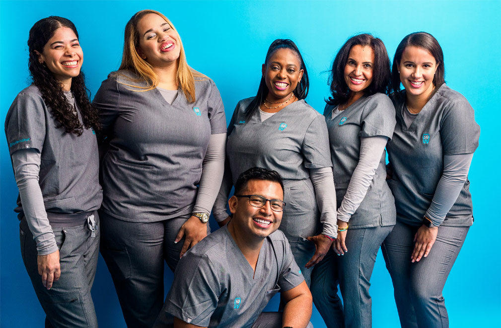 Sky Dental Assistant team: A diverse group of five women and one man smiling. They wear gray Sky Dental uniforms.