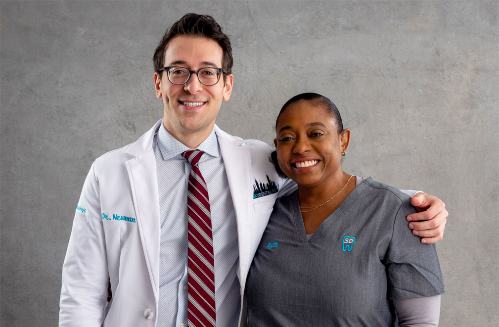 Dr. Ross Newman and Dental Assistant stand side by side, smiling, his arm around her shoulders.