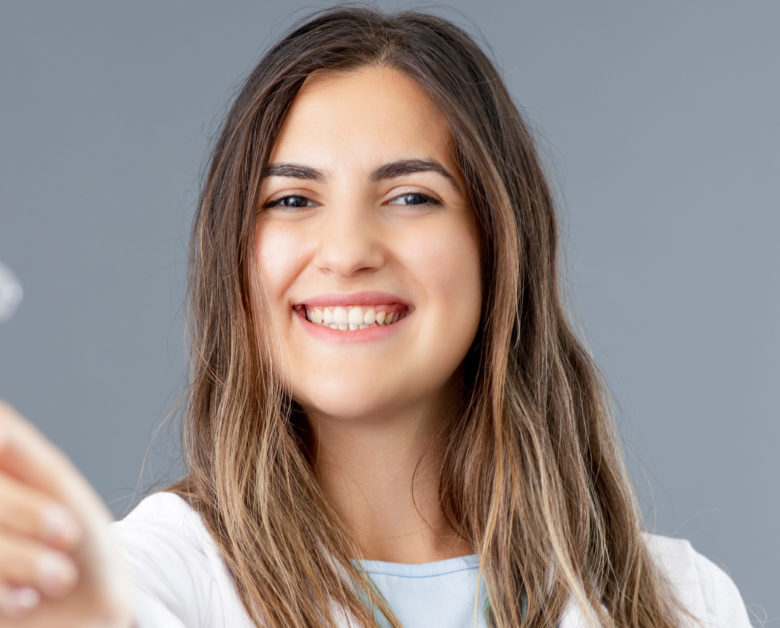 Woman smiles, holding out Invisalign tray. Sky Dental offers Invisalign NYC.