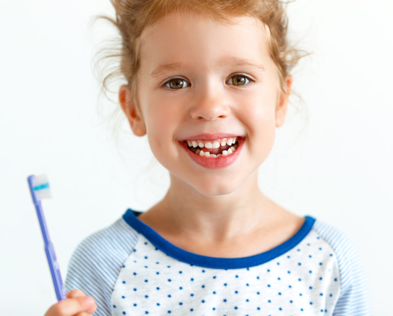 Happy girl, about 7, holds toothbrush and smiles, revealing two missing front bottom teeth.