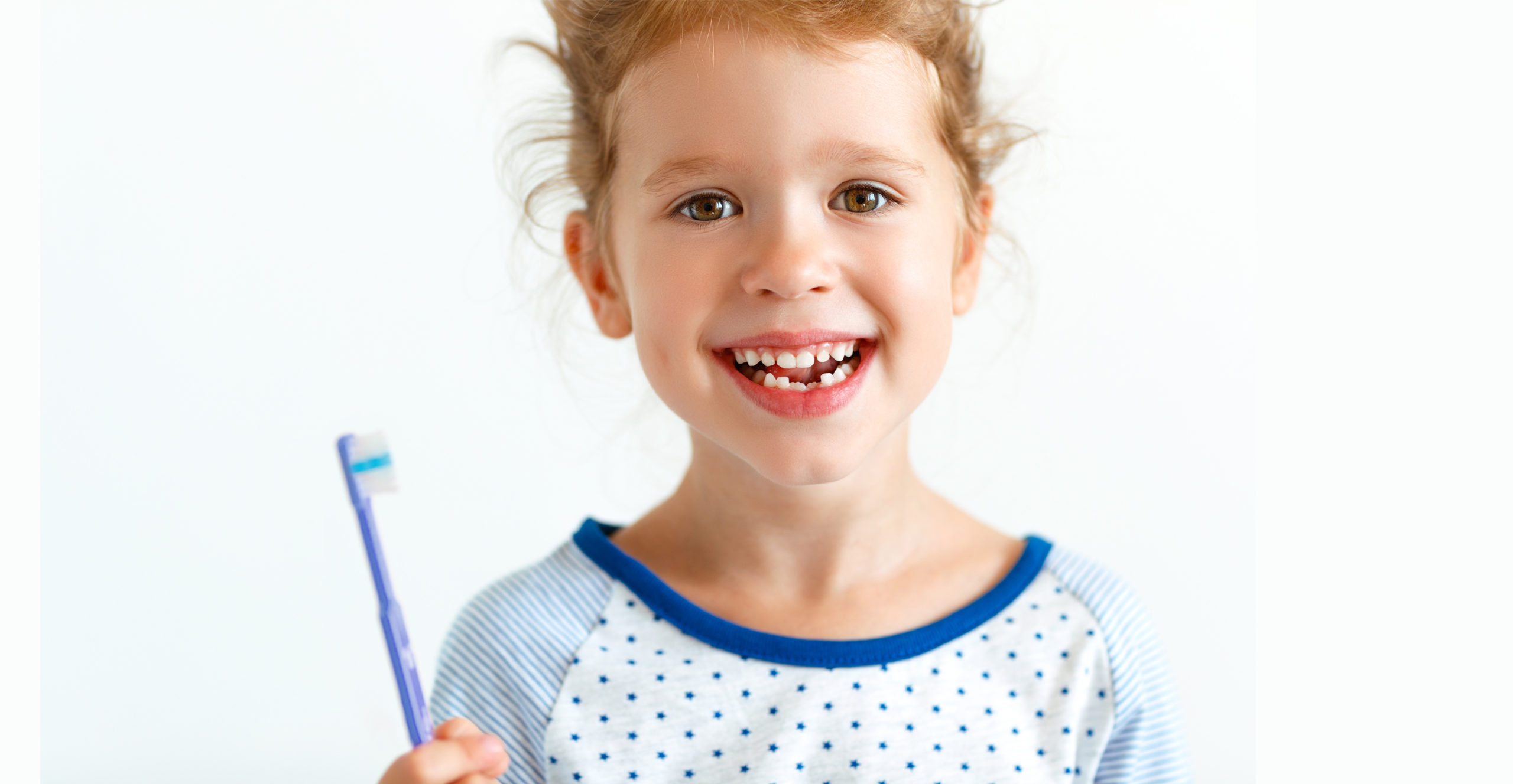 Happy girl, about 7, holds toothbrush and smiles, revealing two missing front bottom teeth.
