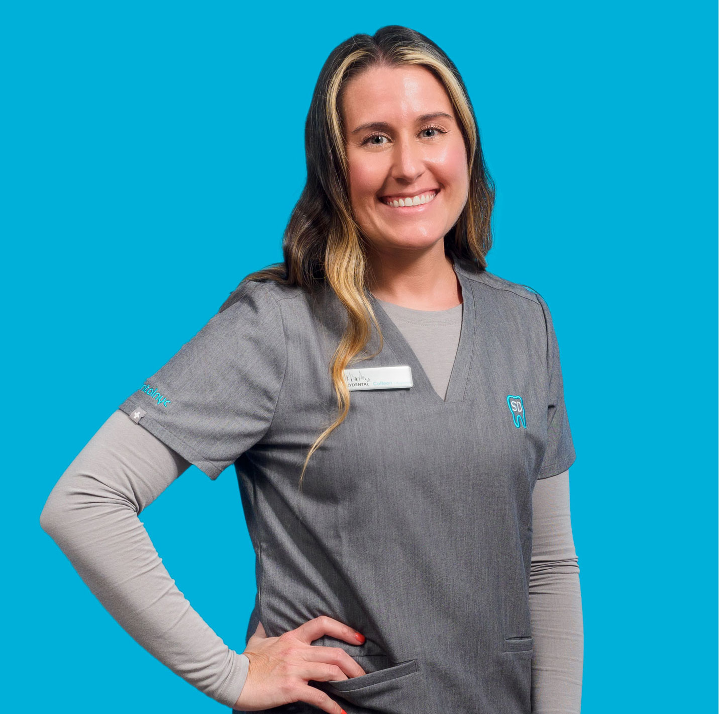 Colleen, hygienist at Sky Dental poses against sky-blue background, hand on hip, smiling.