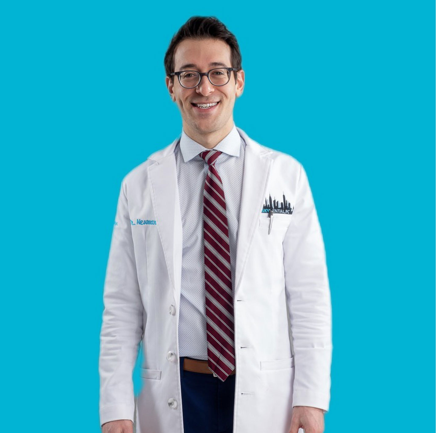 Dr. Newman of Sky Dental—cosmetic and general dentist NYC--wears a white dentist coat, poses against a sky-blue background.