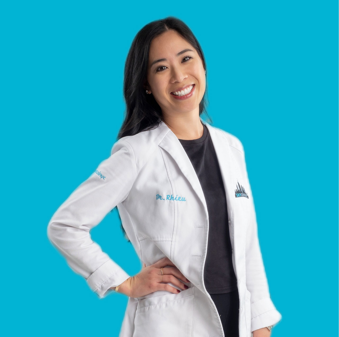 Dr. Wonnie Rhieu of Sky Dental, cosmetic and general dentist. She wears a white dental coat, hand on hip, smiling.