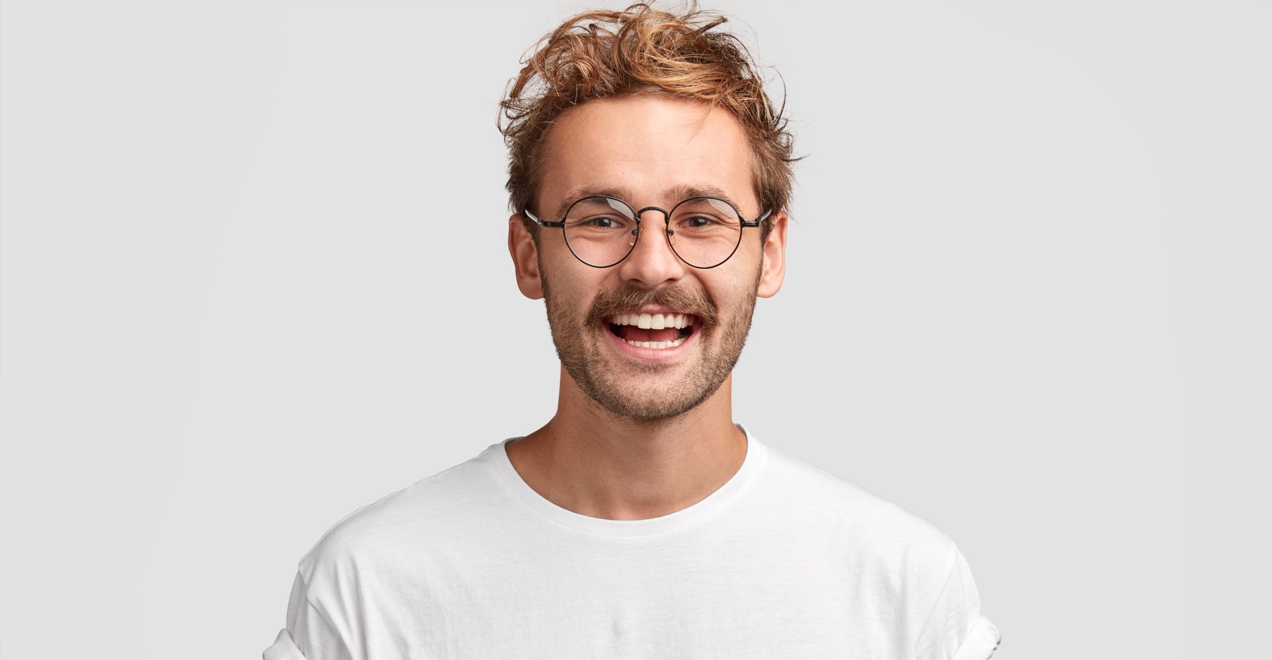 30-something hip man with round-frame glasses joyfully shows a bright white smile.